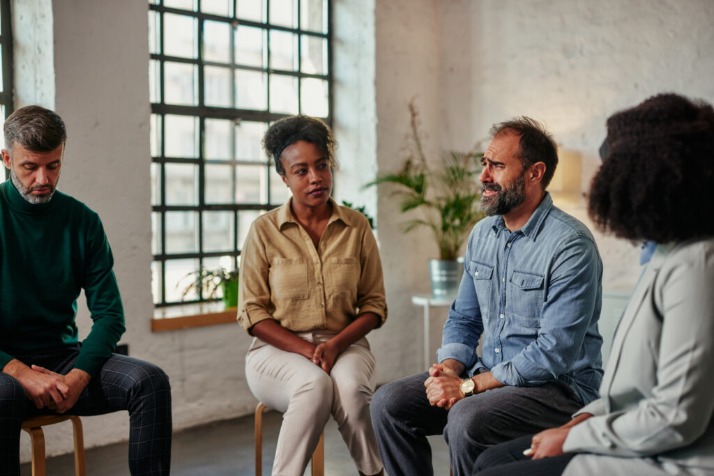 As they sit in a circle, the diverse members of the support group have a discussion.